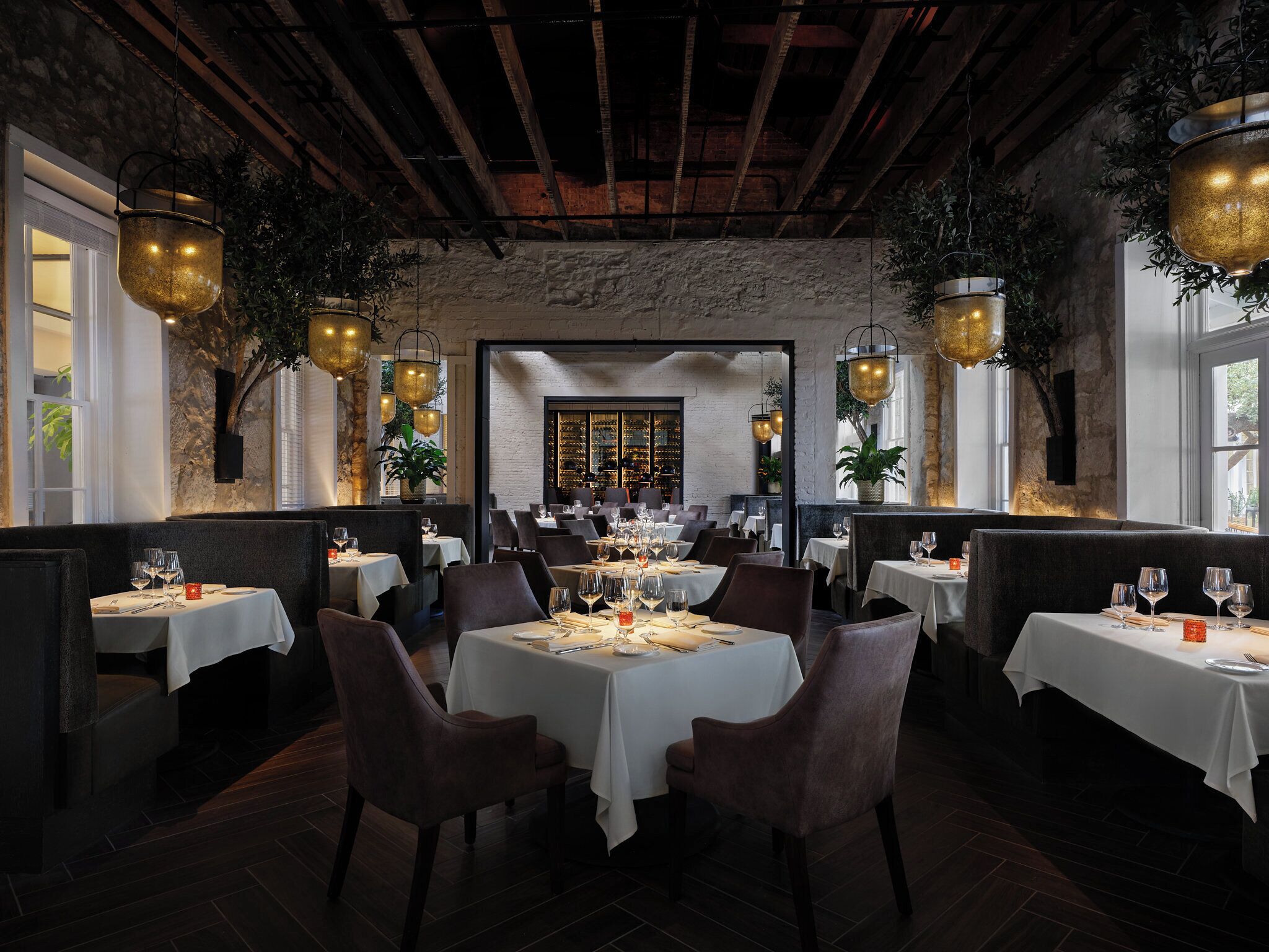 Un restaurante con varias mesas y cabinas, paredes de piedra y lámparas doradas colgantes.