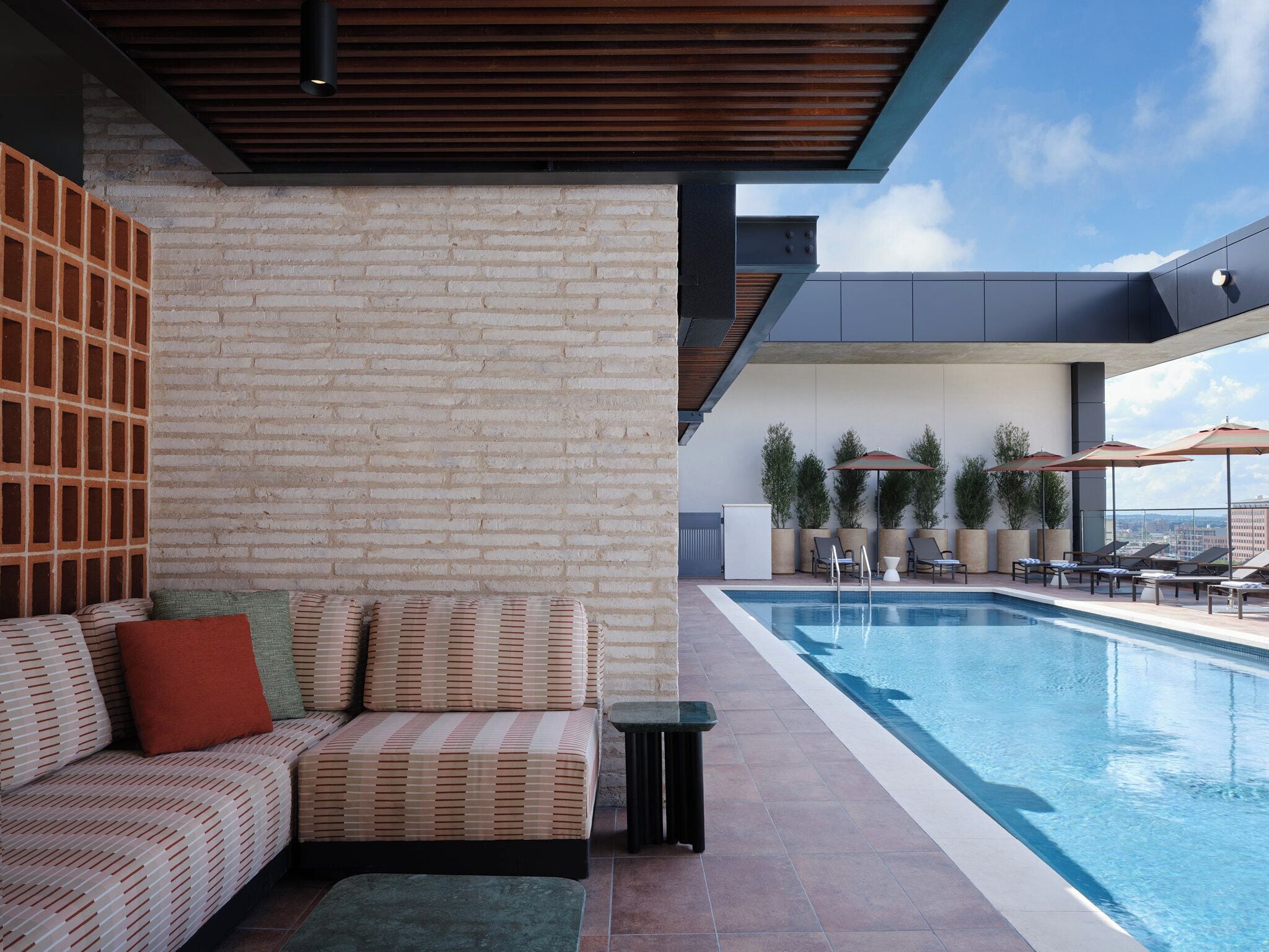 Un área de piscina moderna al aire libre con pared de ladrillo, un sofá y sillones de descanso.