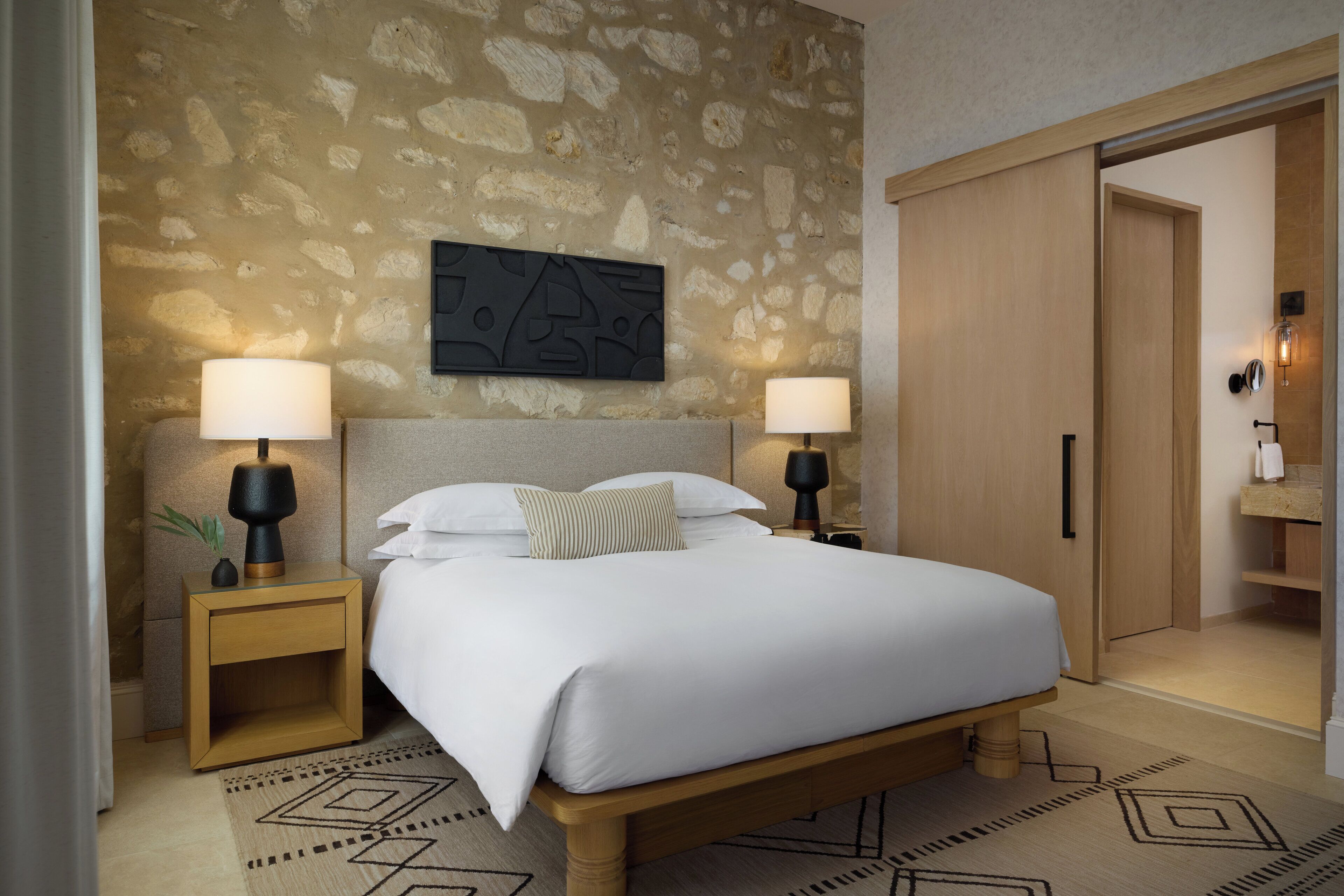 Une chambre à coucher bien aménagée, avec un grand lit, deux tables de chevet avec des lampes, un mur en pierre et une armoire en bois.