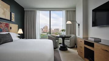A hotel room with a large bed, a desk with a TV, a chair, and a view of the cityscape.