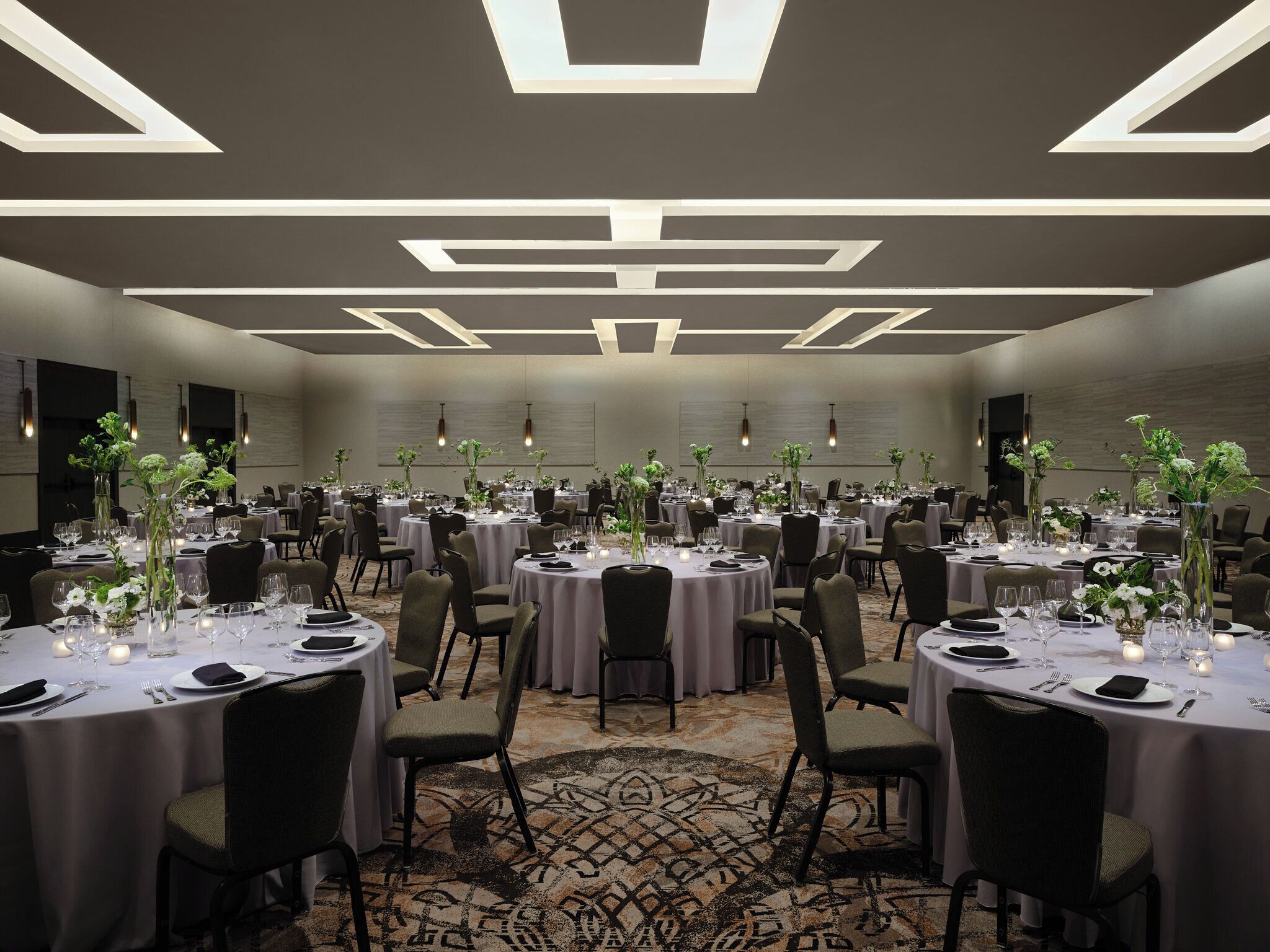 A large banquet hall with round tables, each set with white tablecloths, chairs, and floral centerpieces.