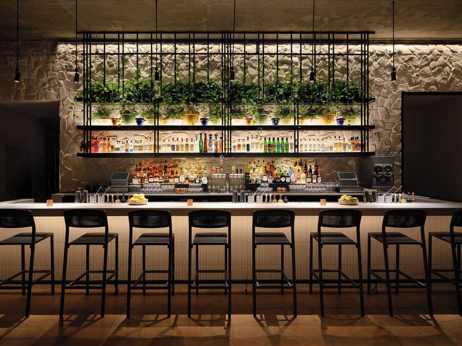 Zona de bar con pared de piedra, varios estantes llenos de botellas y taburetes.