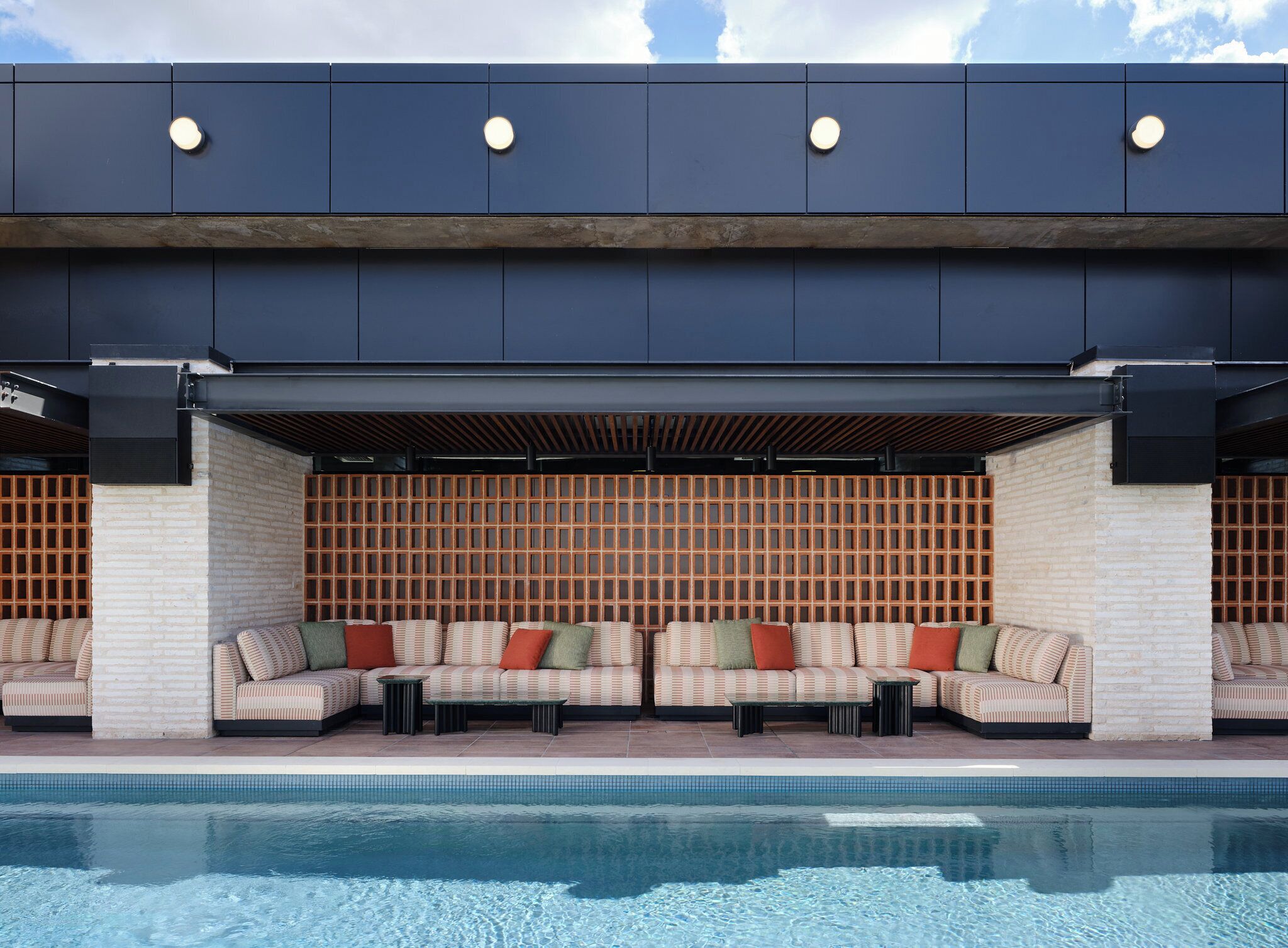 A modern outdoor seating area with a pool, featuring a brick wall and wooden slats.