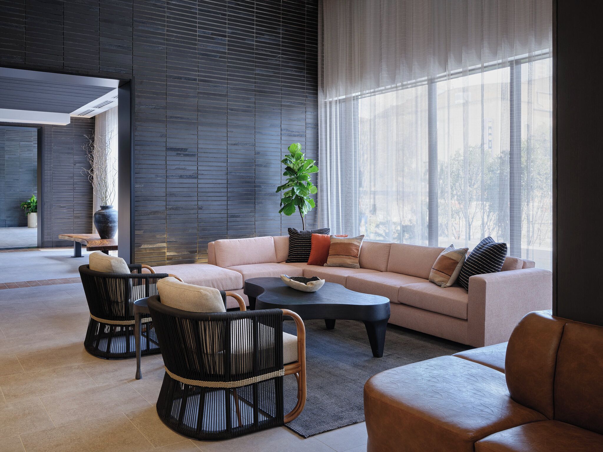 Un salon moderne avec un canapé d’angle, deux fauteuils, une table basse et une grande fenêtre agrémentée de rideaux légers.