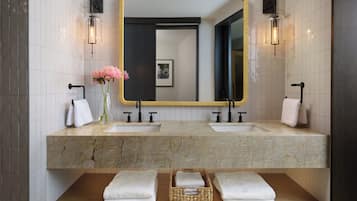A modern bathroom with two sinks, a large mirror, and a wooden shelf with towels.