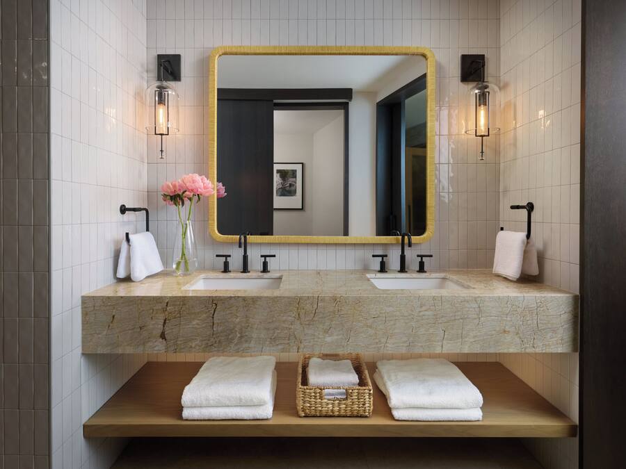A modern bathroom with two sinks, a large mirror, and a wooden shelf with towels.