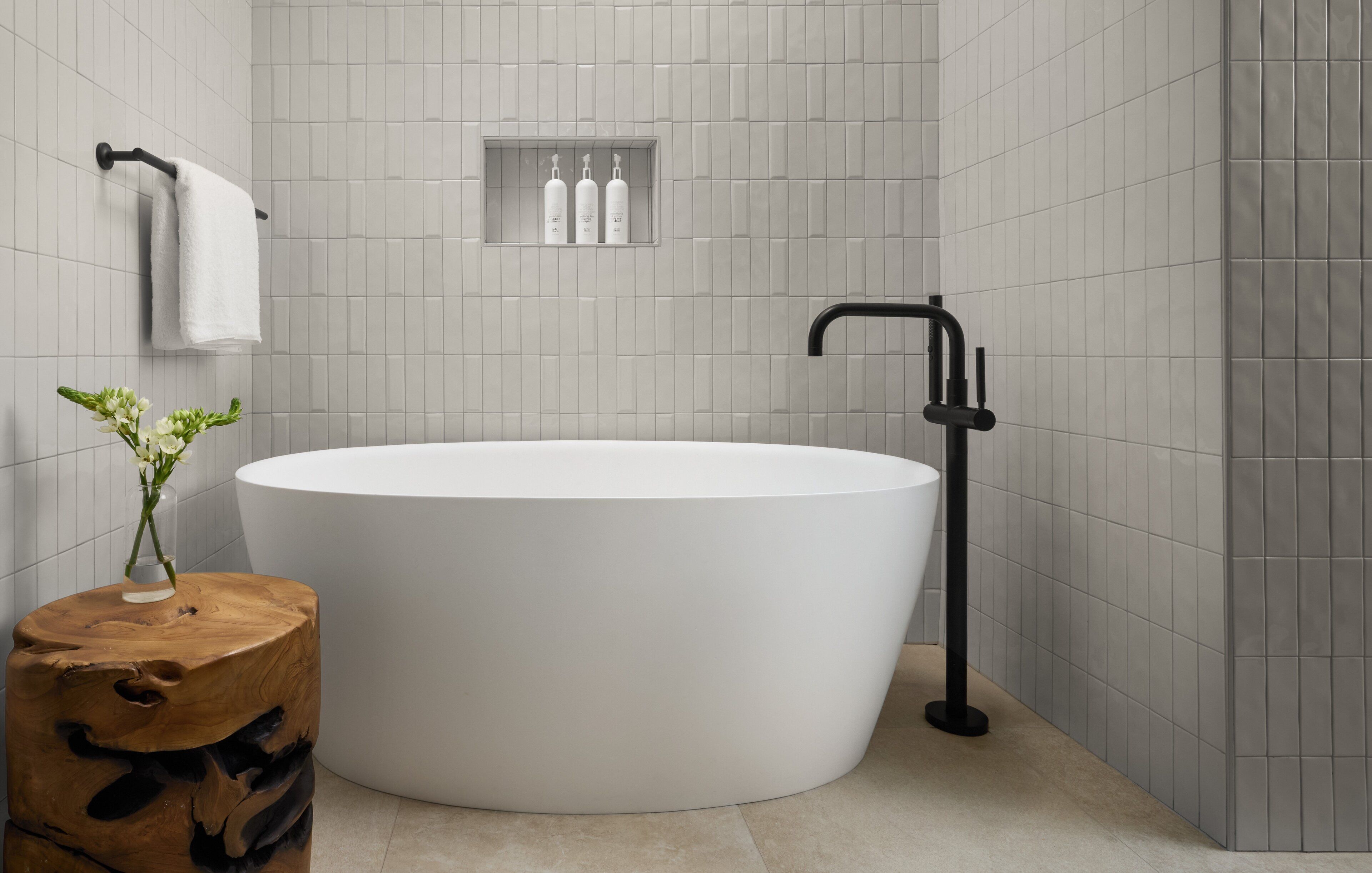 Un baño moderno con una bañera independiente, un taburete de madera, un perchero y un estante con artículos de aseo.