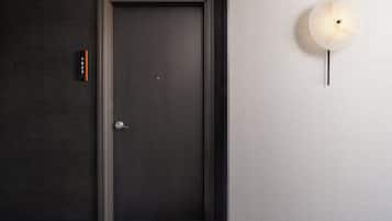 A dark wooden door with a silver handle, a small sign with numbers, and a wall-mounted light fixture.