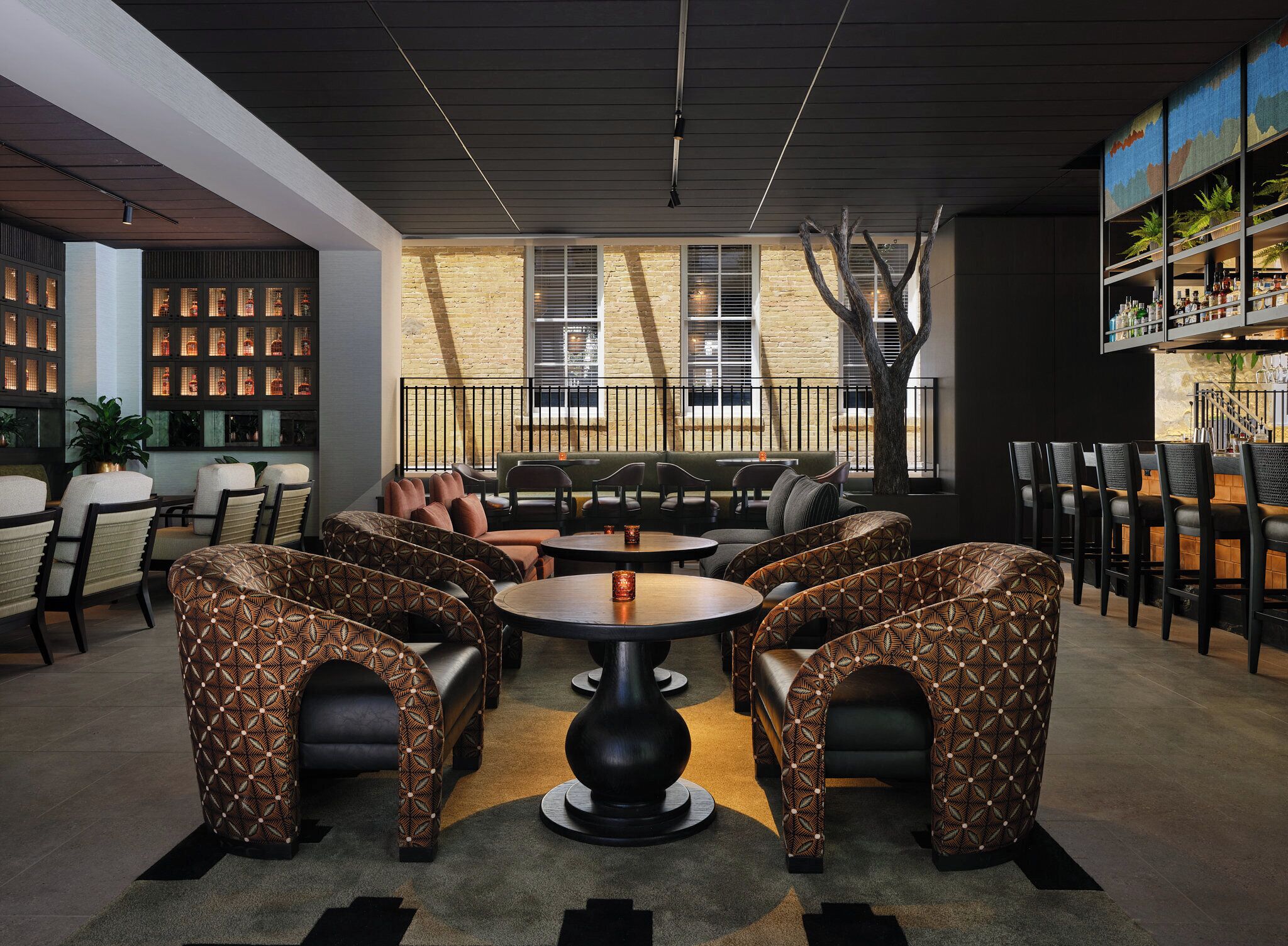 A modern lounge area with patterned seating, a central table, and a staircase leading to an upper level.