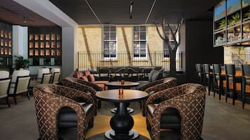 A modern lounge area with patterned seating, a central table, and a staircase leading to an upper level.