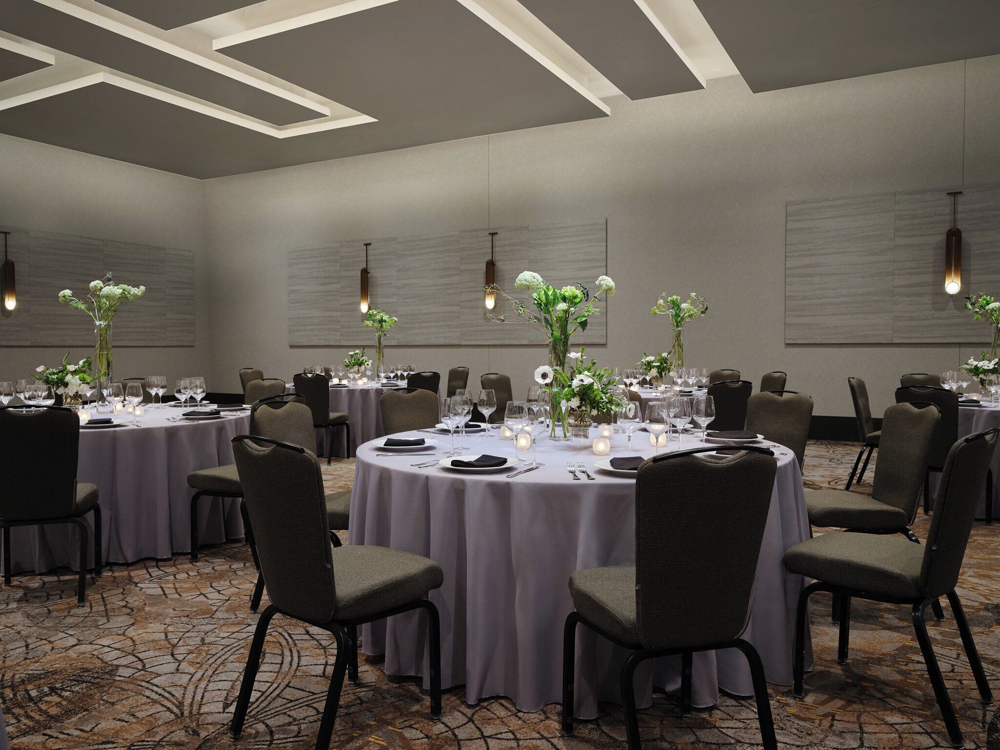 Un salón de conferencias con mesas redondas, sillas y centros de mesa con flores.