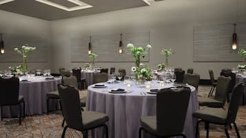 Un salón de conferencias con mesas redondas, sillas y centros de mesa con flores.