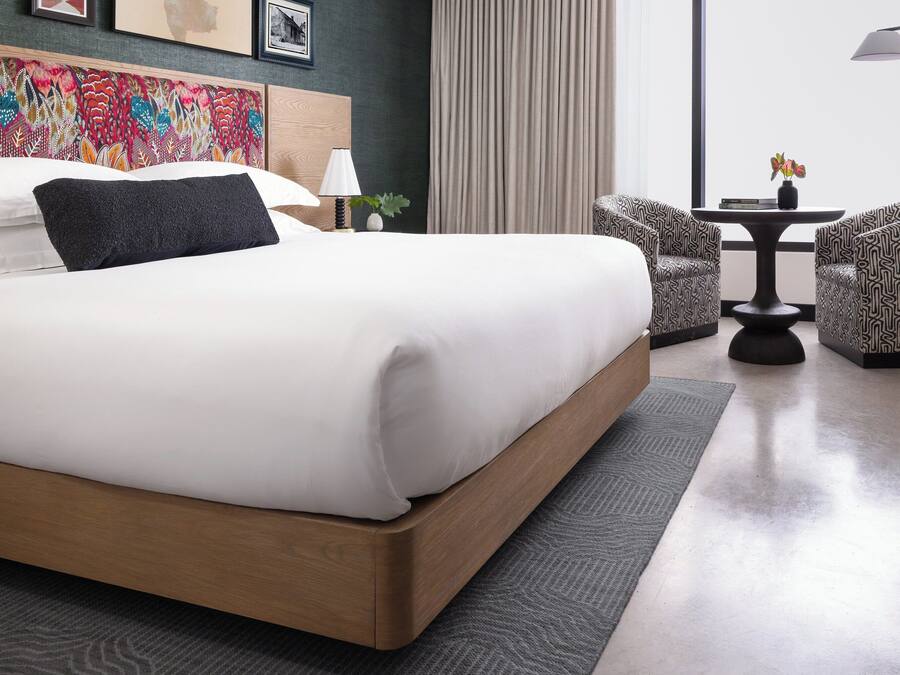 A modern hotel room with a large bed, a small table with chairs, and a decorative headboard.