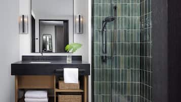 Un baño moderno con un lavabo negro, un espejo, una ducha con puerta de vidrio y una planta sobre el lavabo.