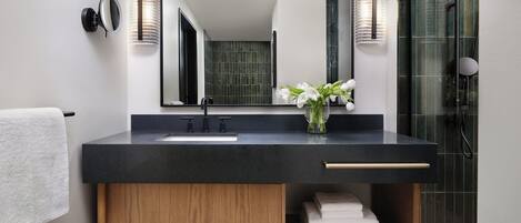 A modern bathroom with a black countertop, a wooden vanity, a large mirror, and a glass shower enclosure.