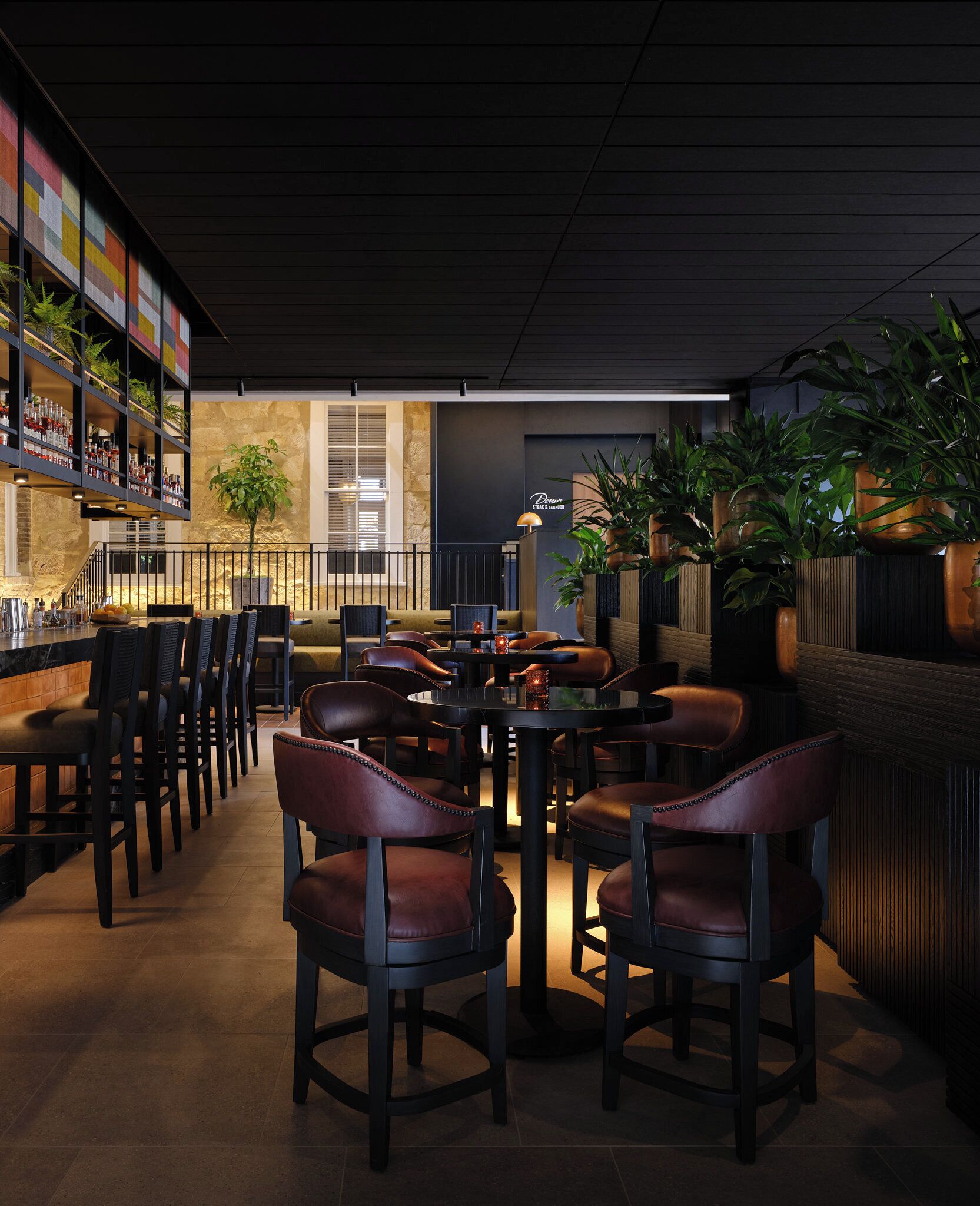 A restaurant interior with a bar area, seating, and plants.