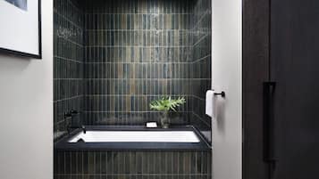 A modern bathroom with dark tiled walls, a black bathtub, and a white towel hanging on the wall.
