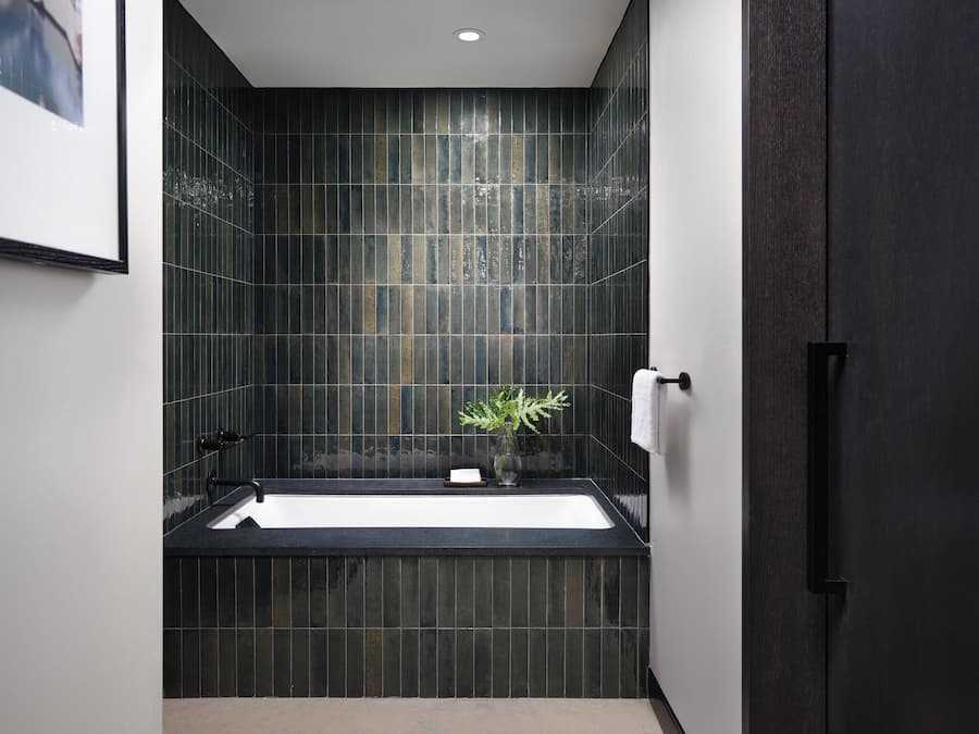 A modern bathroom with dark tiled walls, a black bathtub, and a white towel hanging on the wall.