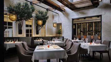 A restaurant with multiple tables set for dining, featuring a brick wall and hanging plants.
