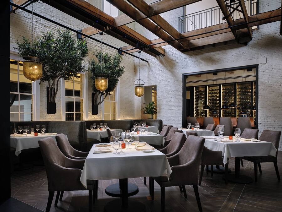 A restaurant with multiple tables set for dining, featuring a brick wall and hanging plants.