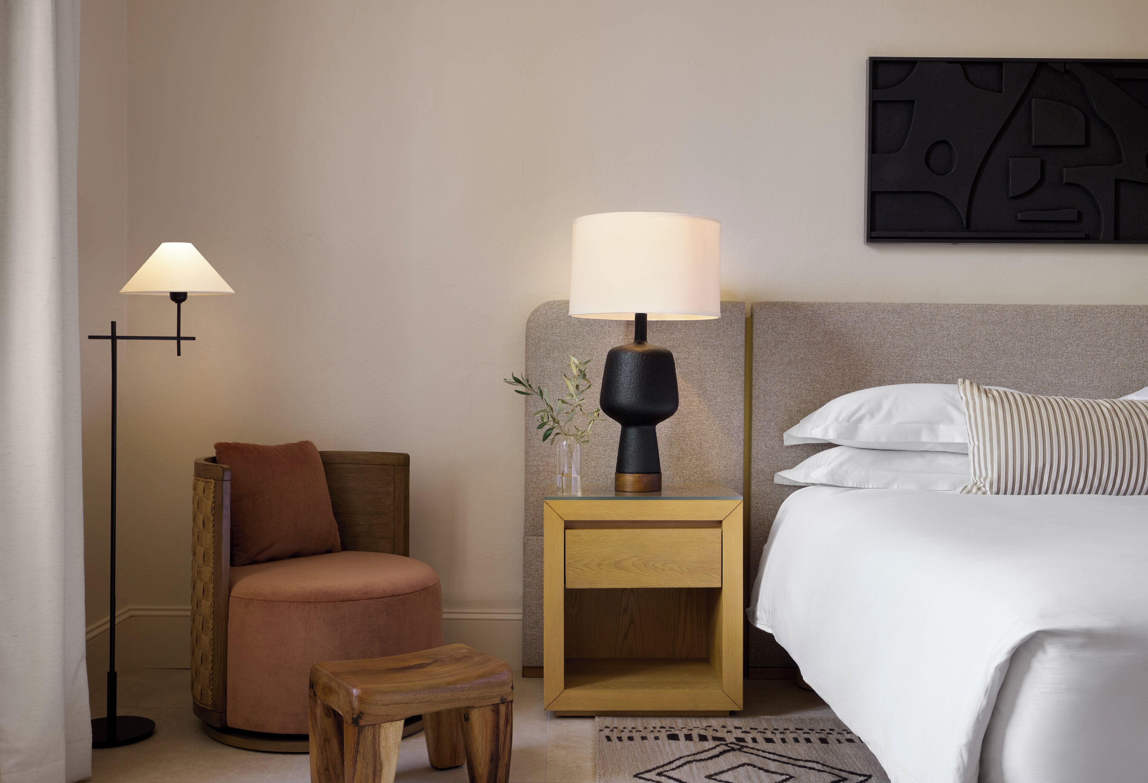 A hotel room with a bed, a nightstand with a lamp, a chair, and a small table.