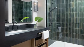 A modern bathroom with a black countertop, two sinks, a large mirror, a shower with a glass door, and a potted plant.