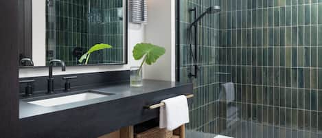 A modern bathroom with a black countertop, two sinks, a large mirror, a shower with a glass door, and a potted plant.