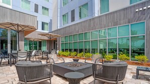 An outdoor patio with wicker furniture, a fire pit, and a large windowed wall. - Drury Inn & Suites Destin Miramar Beach (Miramar Beach)