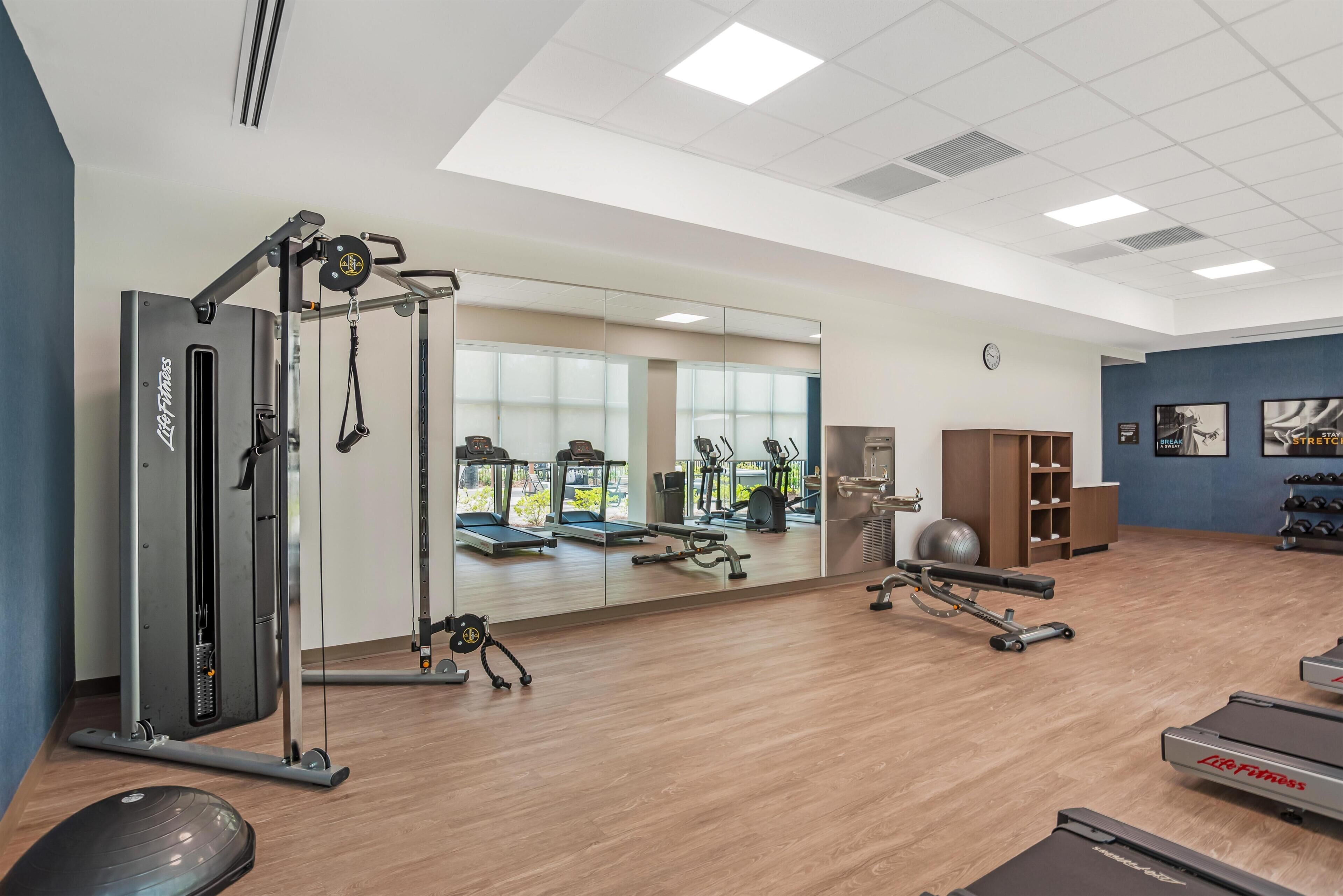 A gym with cardio machines, free weights, and a mirrored wall.