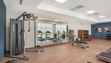 A gym with cardio machines, free weights, and a mirrored wall.
