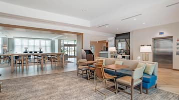 Un vestíbulo de hotel con zona de comedor, un sofá y una cocina al fondo.