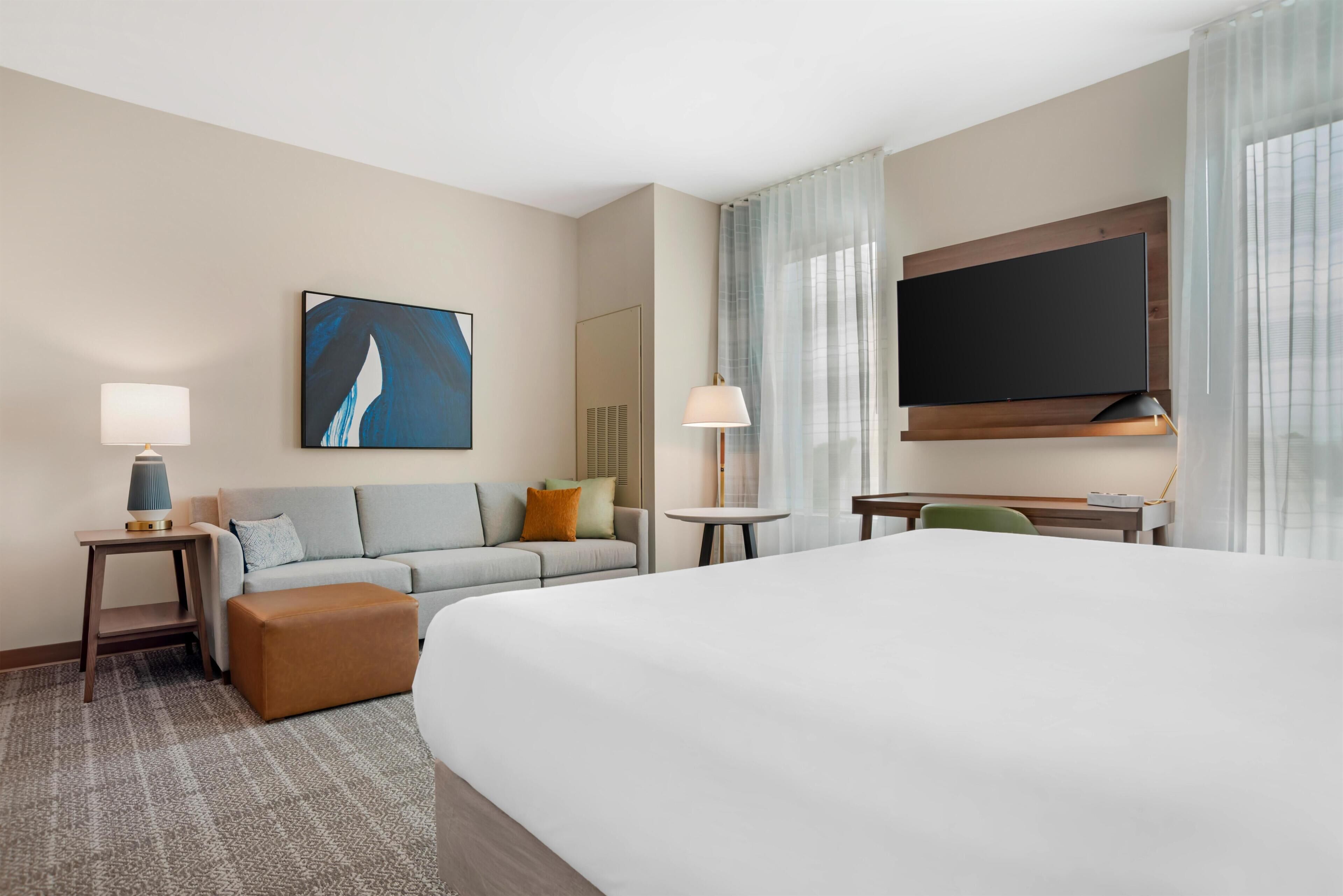 Ein Hotelzimmer mit einem Bett, einem Sofa, einem Schreibtisch, einem Fernseher und einem Bild an der Wand.