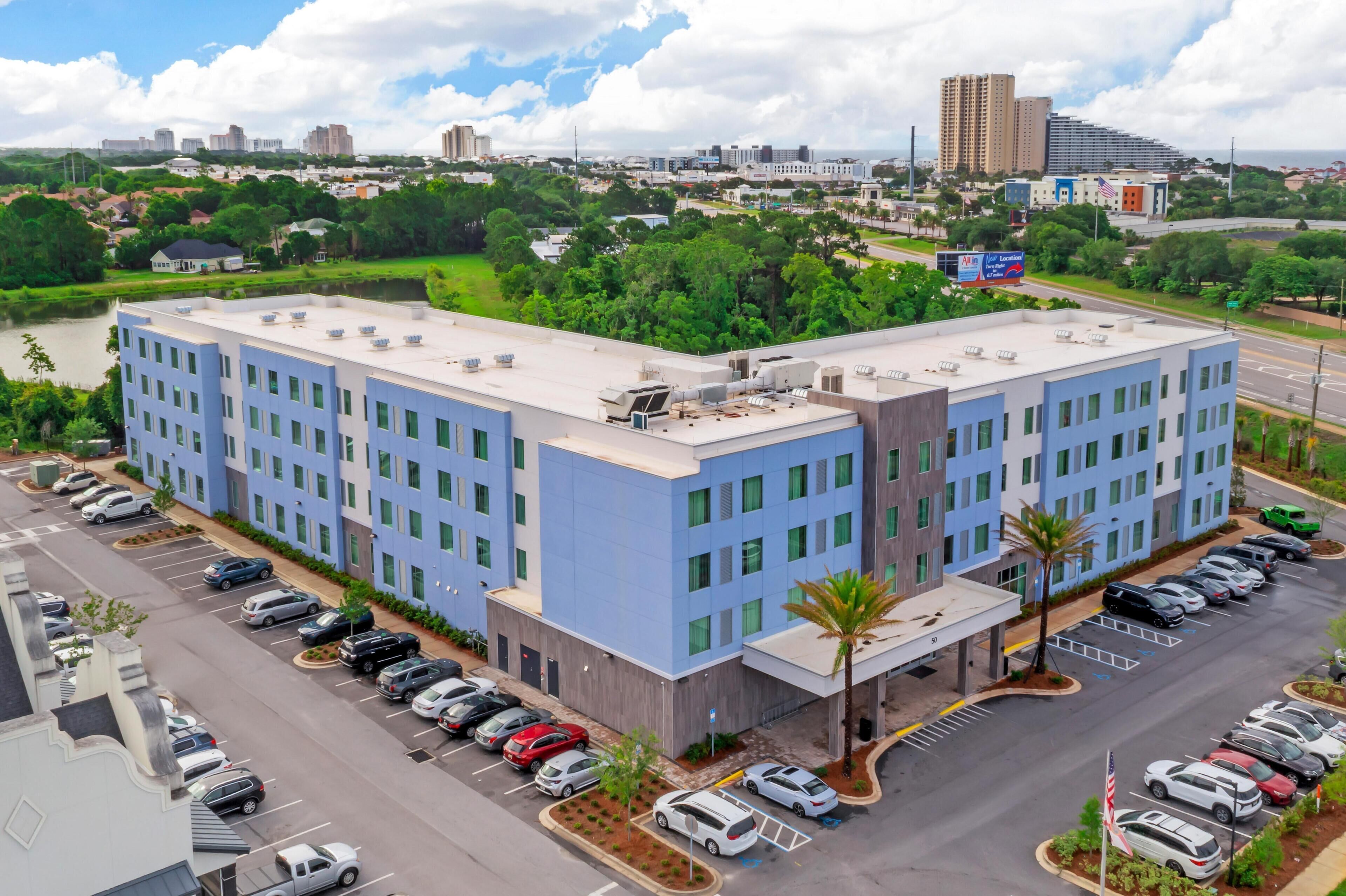 A multi-story hotel with a parking lot, surrounded by greenery and urban buildings.