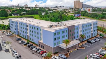 A multi-story hotel with a parking lot, surrounded by greenery and urban buildings.