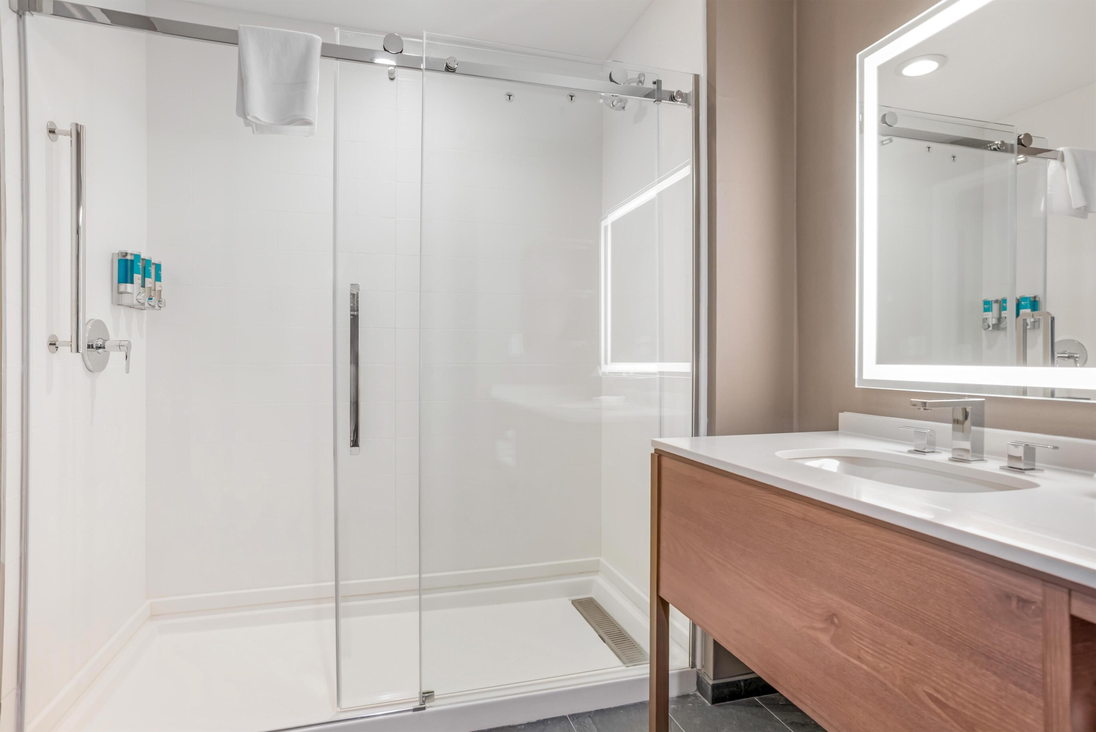 Un baño moderno con cabina de ducha de vidrio, tocador de madera con lavabo y un espejo grande.