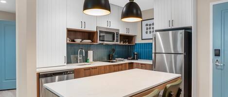 A modern kitchen with white cabinets, a stainless steel refrigerator, a microwave, and a large island with bar stools.