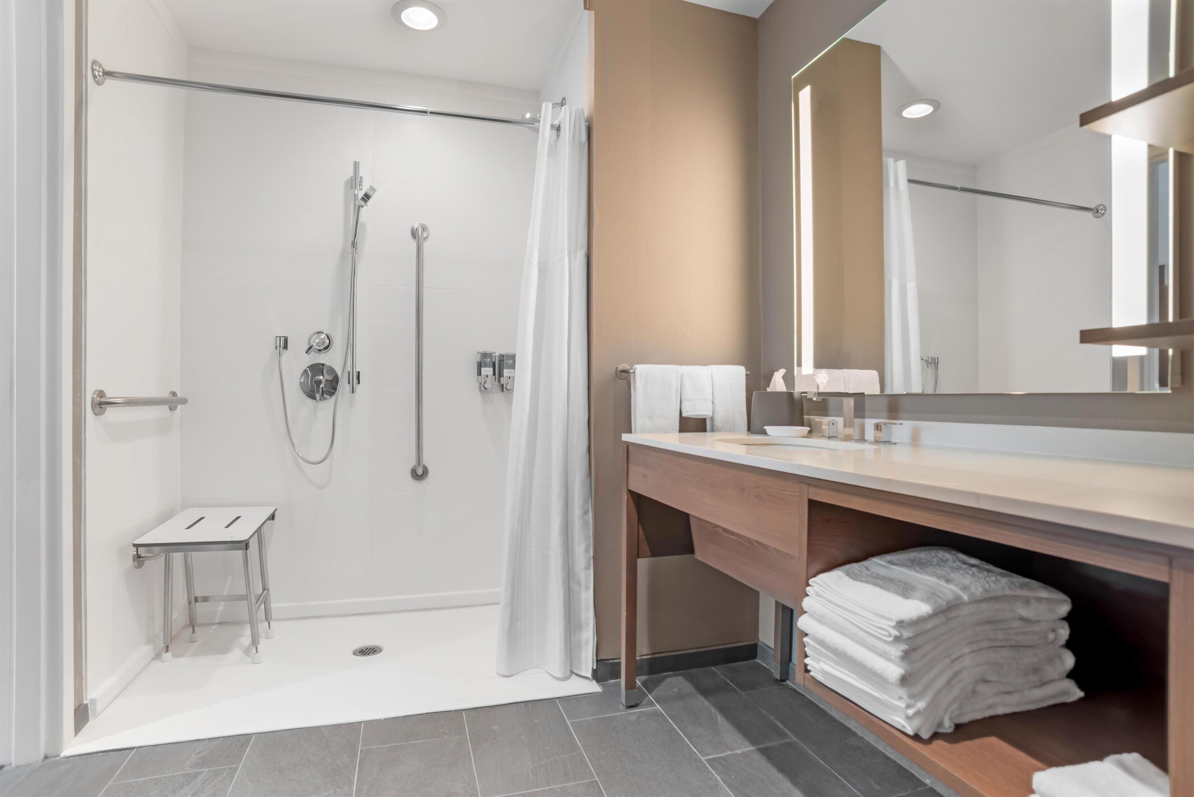Ein modernes Badezimmer mit Dusche, Waschtisch und Spiegel sowie einem kleinen Hocker.