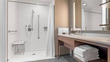 Un baño moderno con ducha, tocador con espejo y un taburete pequeño.