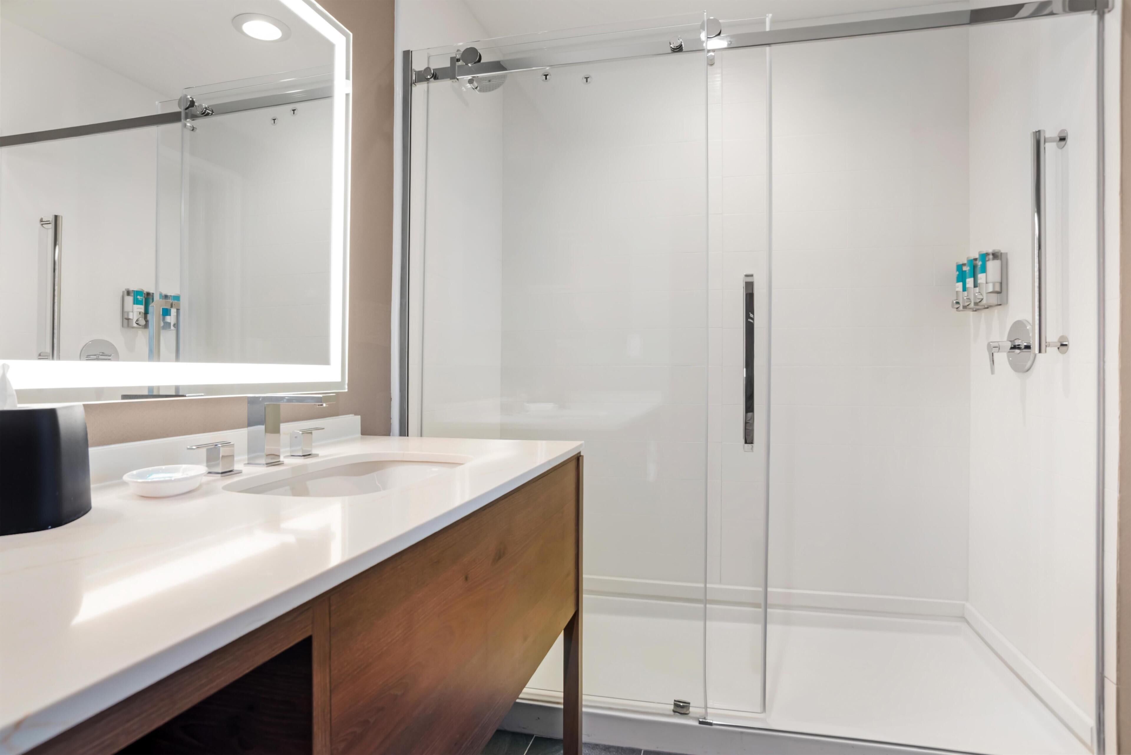 A modern bathroom with a glass-enclosed shower, a large mirror, and a wooden vanity.
