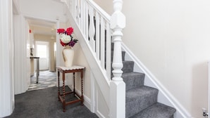 A staircase with white balusters and a wooden side table with a vase of flowers. - Superior three bedroom house with sea view (Swansea)