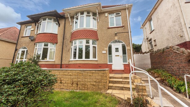 A two-story house with a brick facade, a red-tiled roof, and a small front garden. - Superior three bedroom house with sea view (Swansea)