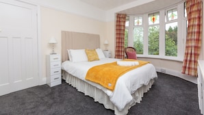A bedroom with a large bed, a nightstand, a chair, and a window with curtains. - Superior three bedroom house with sea view (Swansea)