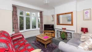 A living room with a sofa, armchair, and a TV. There is a fireplace and a mirror on the wall. - Superior three bedroom house with sea view (Swansea)