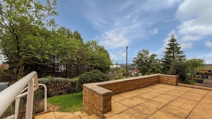 A patio with a brick wall and steps leading up to it, surrounded by greenery and trees. - Superior three bedroom house with sea view (Swansea)