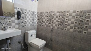 A bathroom with a toilet, sink, and shower. The walls are tiled with a checkered pattern and floral designs. - OSHO Villa Homestay, 5 minutes to the Jaipur Airport, Garden View AC Rooms,  (Jaipur)