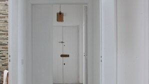 Un corridoio con pareti bianche e pavimento piastrellato, che conduce a una porta con una lanterna a sospensione.