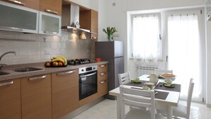 Una cucina moderna con mobili in legno, un frigorifero in acciaio inox e un'area pranzo con sedie bianche e un tavolo.
