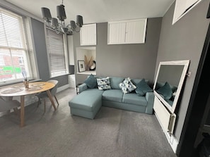 A living room with a sectional sofa, a dining table, and a radiator.