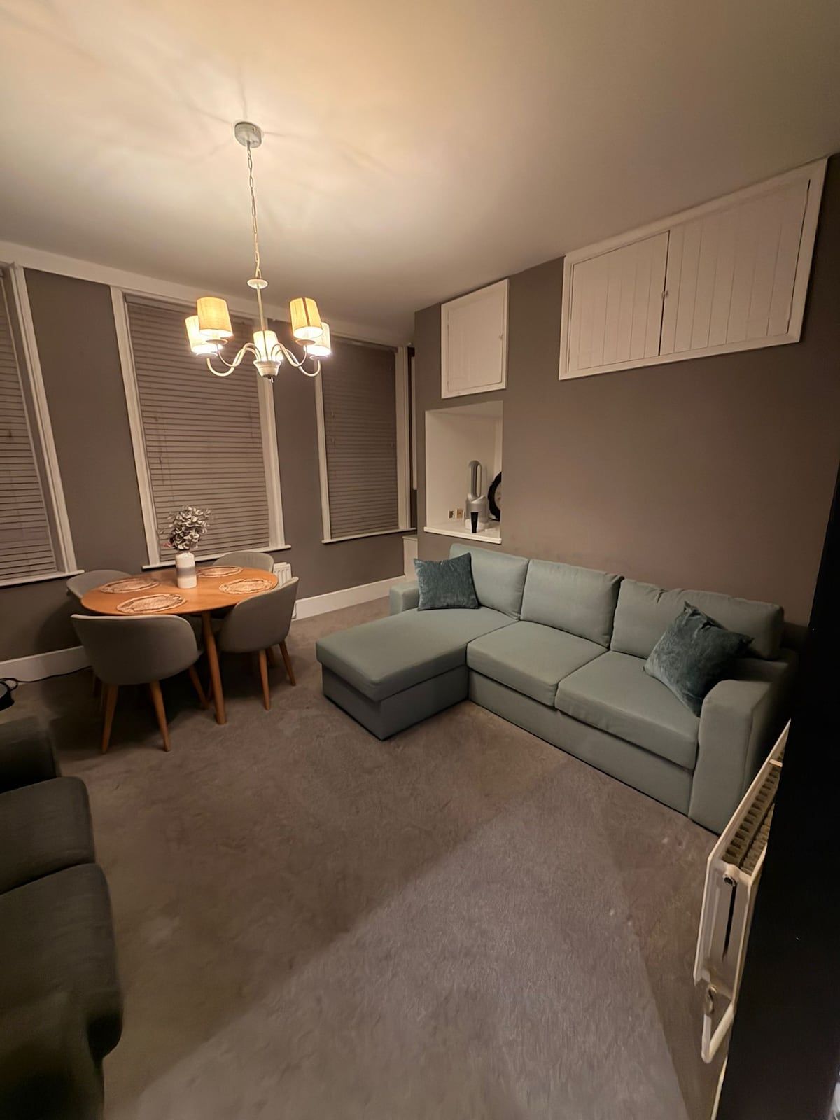 Una sala de estar con un sofá modular, una mesa de comedor con sillas, una araña y un ventilador de techo.