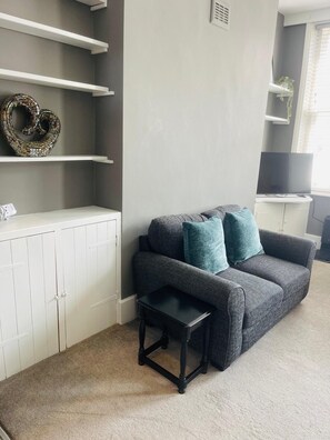 A living room with a grey sofa, teal cushions, a small black table, white cabinets, and a TV on a stand. - 1-Bedroom Flat in Islington! (Greater London)
